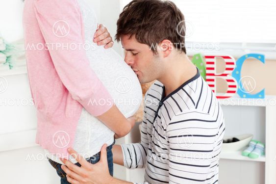 Portrait of a kind man kissing his pregnant wife's belly