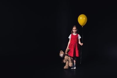 sad child with yellow balloon and teddy bear looking at...