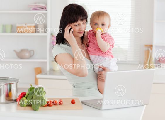 Good looking brunette woman on the phone while holding her baby in her arms