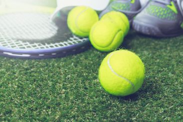 Bright yellow tennis balls and a racket on green grass...