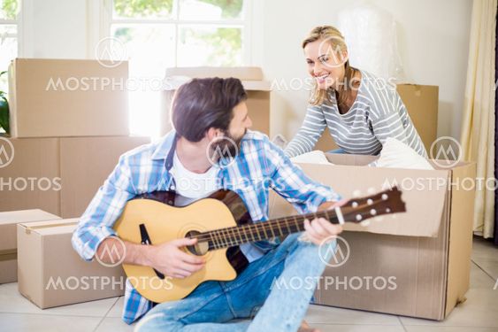 Man playing a guitar while woman unpackaging cardboard...