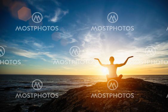 young woman practicing yoga on the beach at sunset.
