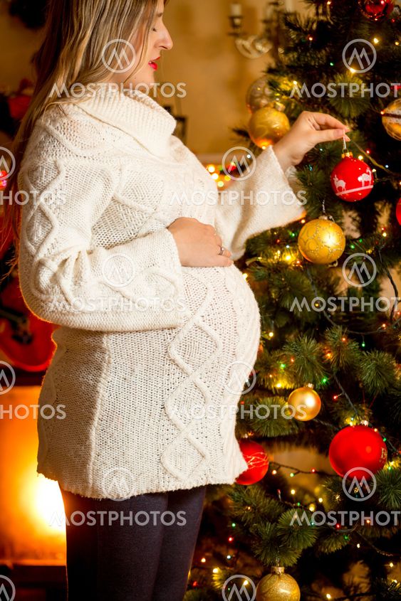 Closeup of pregnant woman decorating Christmas tree at...