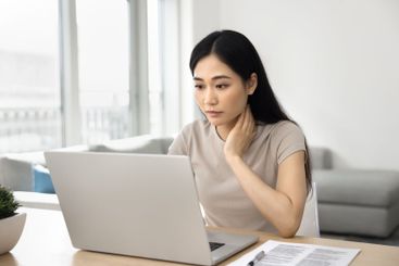 Young serious Asian woman sit at table and using laptop