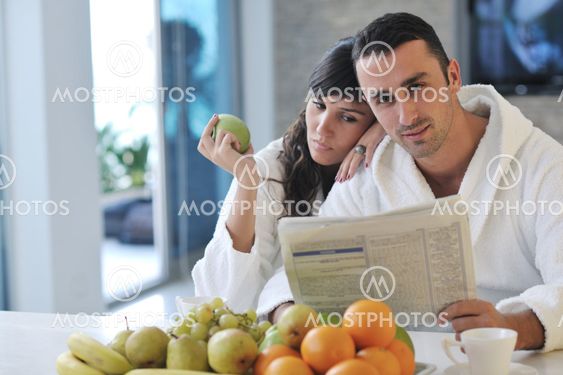Happy couple reading the newspaper in the kitchen at breakfast