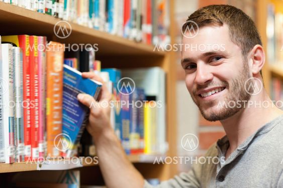 Smiling male student picking a book