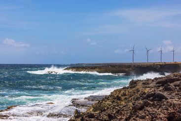 Waves crashing against rocky coastline near wind turbines 