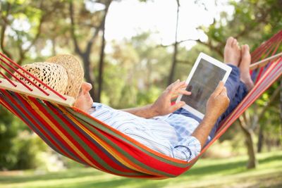 Senior Man Relaxing In Hammock With  E-Book