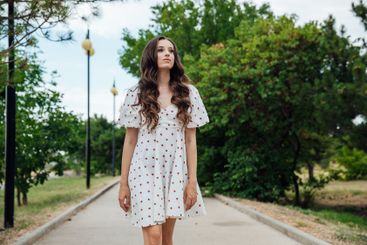 brunette woman in white polka dot summer dress walking...