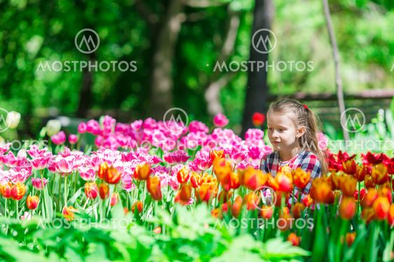Little adorable girl smelling colorful tulips at summer garden