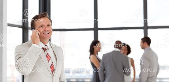 Smiling businessman holding a phone at workplace with his colleagues