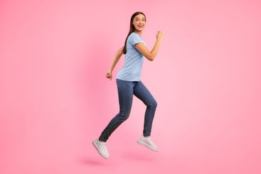 Happy lady jumping and running over yellow studio wall