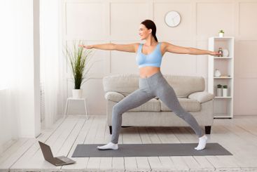Woman Doing Yoga At Laptop Standing In Warrior Pose Indoor