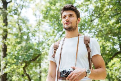 Man with backpack and old photo camera standing in forest
