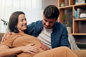 Pregnant woman, man and touch stomach on sofa, smile or...