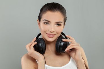Beautiful brunette woman with headphones smiling on gray...