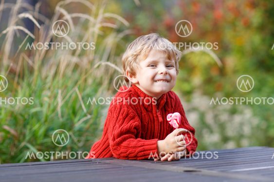 Funny little preschool boy sitting on a wall in late summer evening park, outdoors