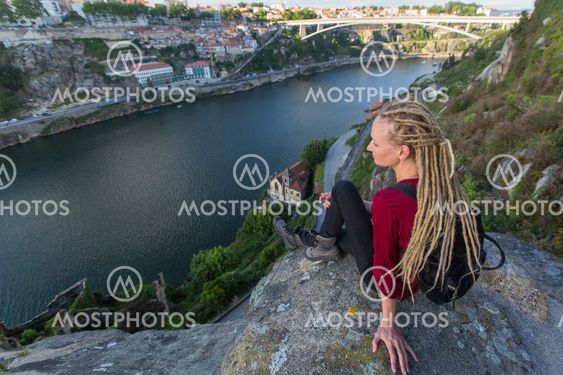 Young woman with backpack sitting on cliff's edge and looking at the river.