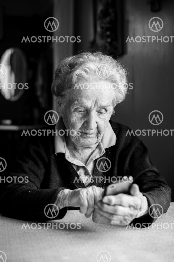 Old woman takes on smartphone sitting at the table in the...