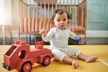 Baby boy playing with wooden car toys on floor in...