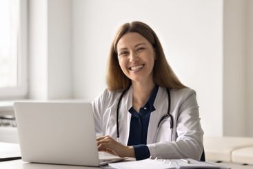 Young doctor sitting at desk by notebook looking at camera