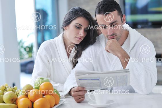 Happy couple reading the newspaper in the kitchen at breakfast