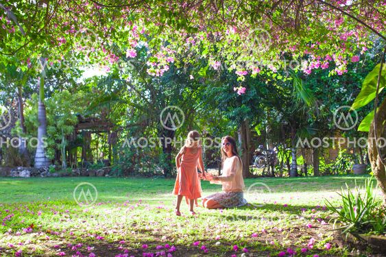 Little girl with mother sitting in the lush garden and enjoy summer rest