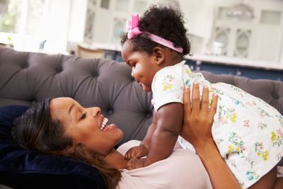Mother lying back holding her toddler daughter on top of...