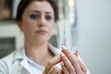 A focused nurse in a white lab coat carefully prepares a...