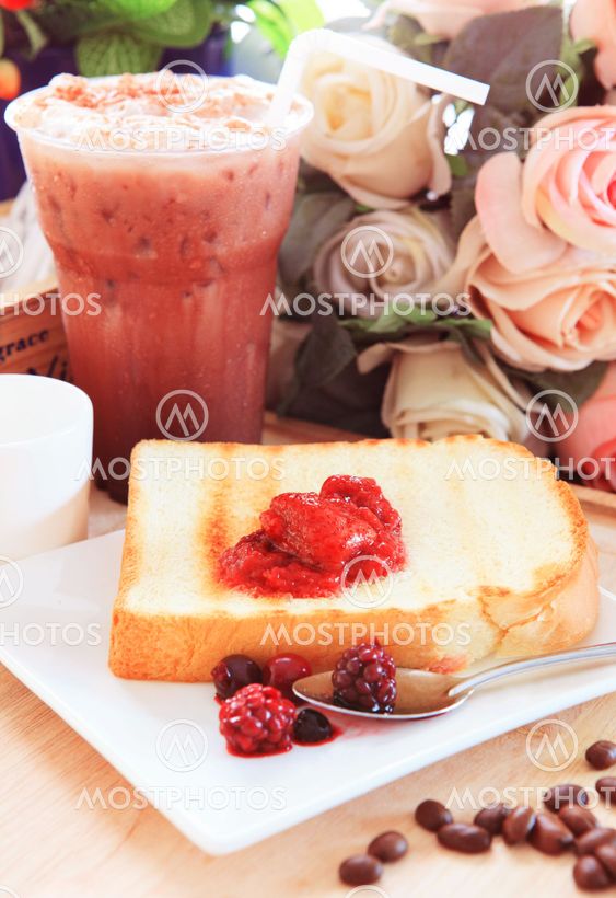 toast bread and sweet strawberry and berry jam in white dish beside cool choclolate on table top ready to eat