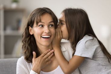 Close up of little daughter sharing secret in moms ear