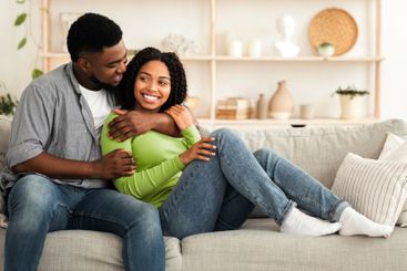 Young Black Couple In Love Cuddling On Couch In Living Room