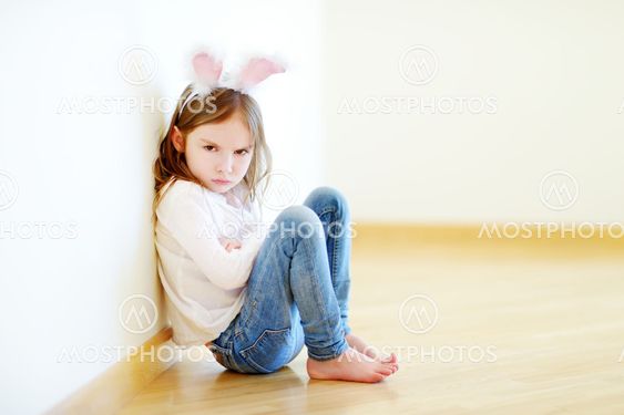 Very angry little girl wearing bunny ears sitting on a...