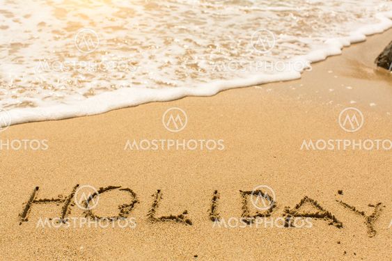 Holiday - word drawn on the sand beach with the soft wave.