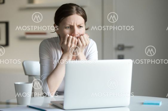 Portrait of a young woman at desk with laptop, fear