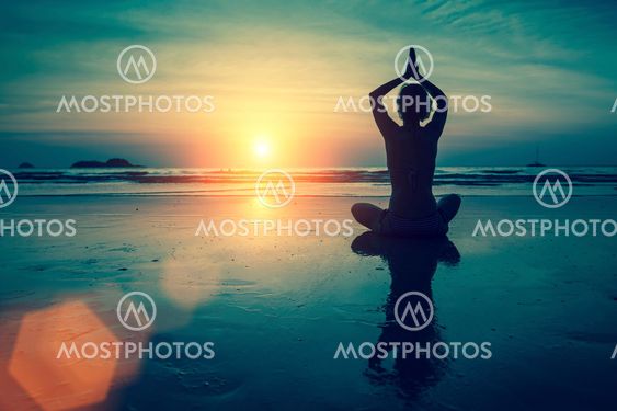 Silhouette of woman practicing yoga in Lotus position at sunset on the sea coast.
