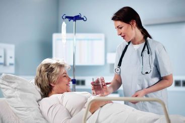 Happy Female Doctor Giving Glass Of Water To Senior Woman