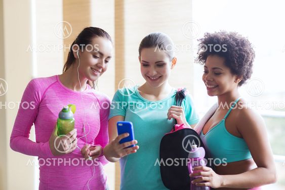 happy women with bottles and smartphone in gym