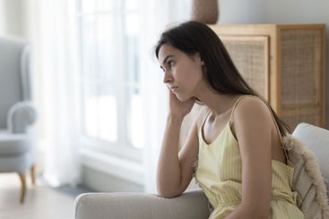 Unhappy teen girl sit on couch propping head with hand