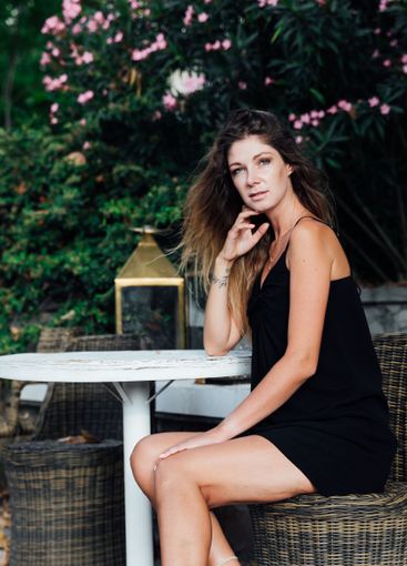 Beautiful slim woman in black summer dress sitting in...
