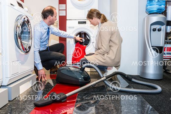 Salesman Showing Washing Machine To Customer In Shop