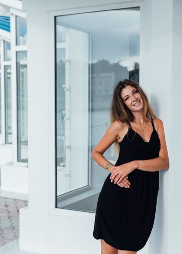 Beautiful slim woman in black summer dress sitting in...