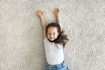 Carefree little girl lying on fluffy carpet with closed...