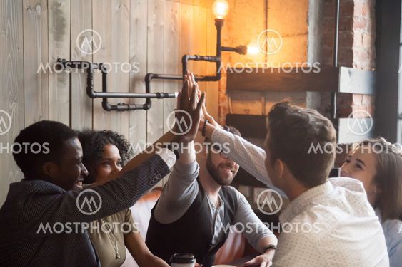 Smiling millennials giving high five during meeting in cafe