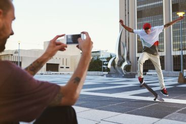 Man, skateboard and picture with camera in city for...