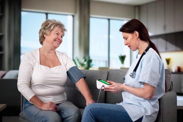 Happy Female Doctor Measuring Senior Patient Blood...