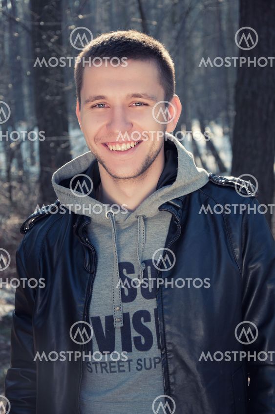 Satisfied smiling young man standing outdoors, in the forest
