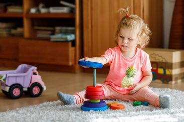 Happy toddler girl sits on a carpet, playing with...