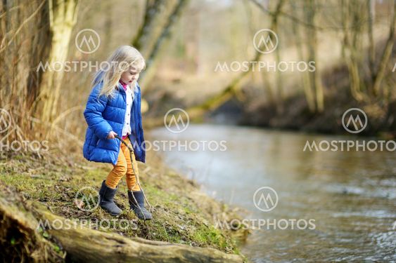 Adorable girl playing with a stick by a river