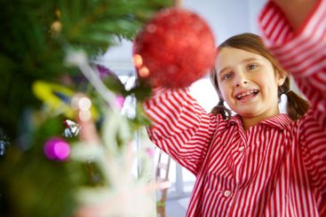 Girl, decoration and baubles on Christmas tree in home,...